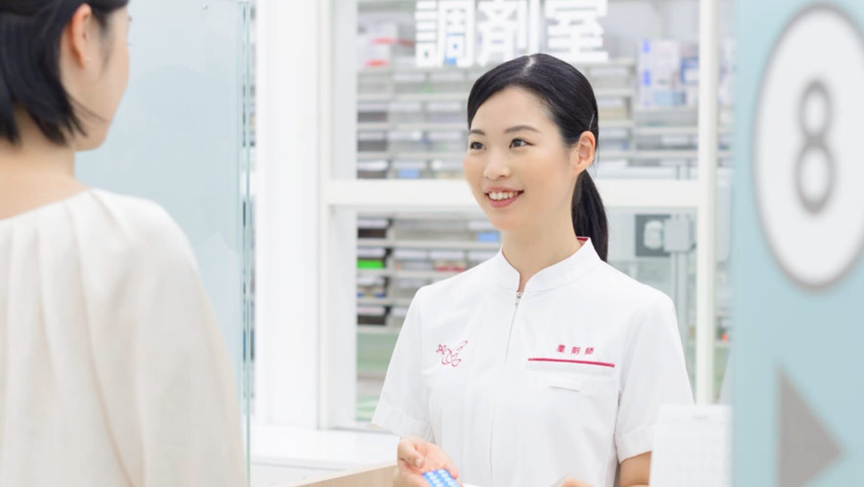薬剤師と患者のイメージ写真。アイン薬局の制服を着た女性の薬剤師が笑顔で薬の説明をしている。