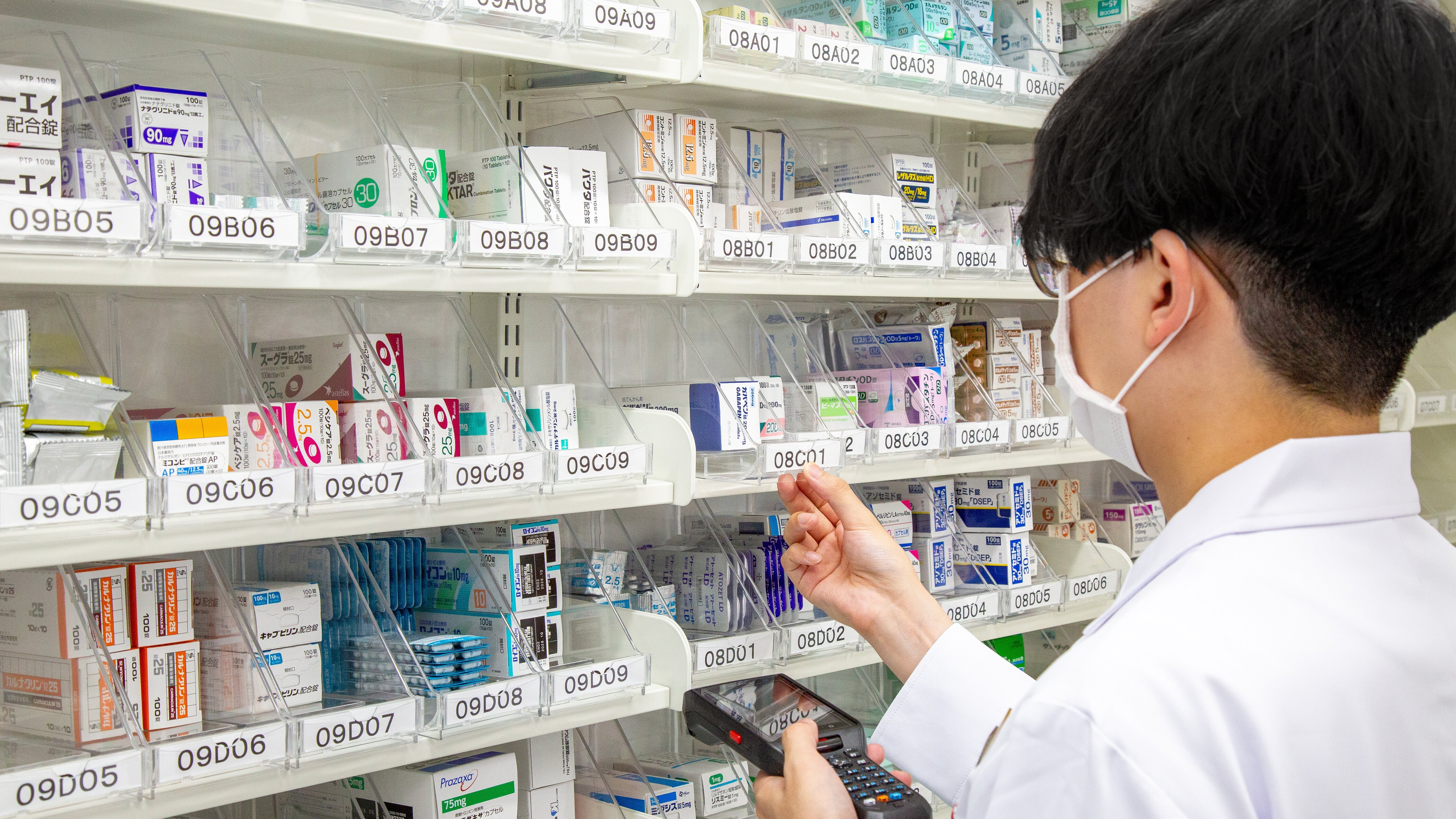 薬剤師が棚から薬品を取り出そうとしている様子の写真。