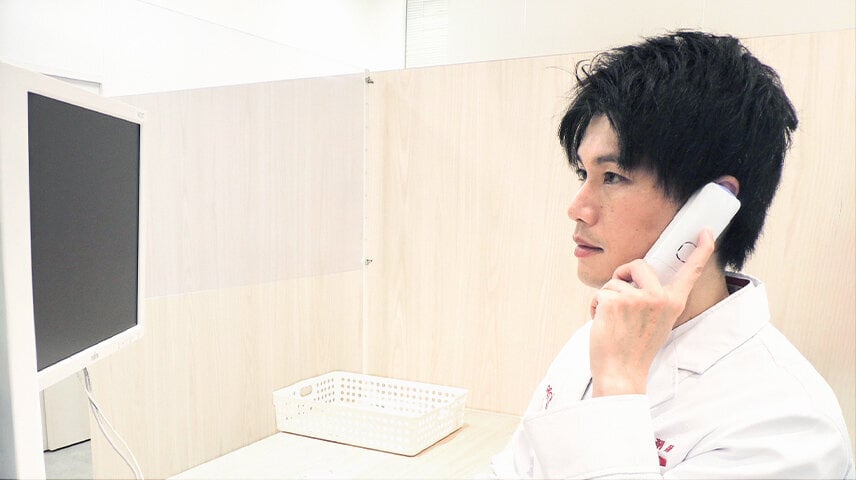 白い服の男性が受話器を耳に当てている様子。