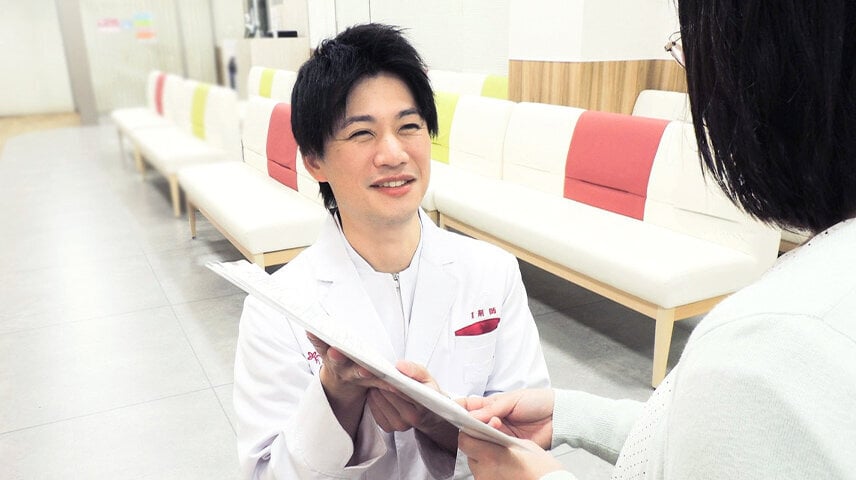 白衣の男性が書類を差し出し、女性が受け取っている様子。