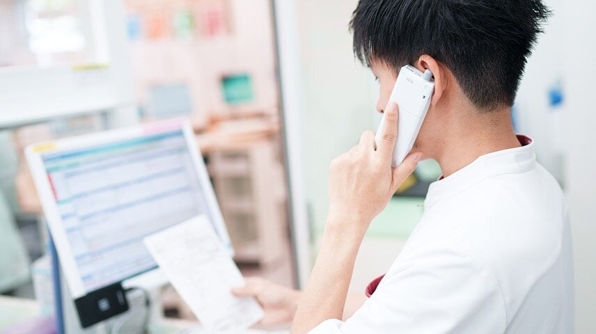 白衣の人物が受話器を耳に当てながら、書類を見ている様子。